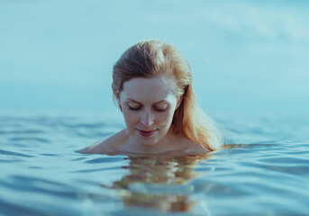 Beautiful blond young woman looking at her reflection in the water