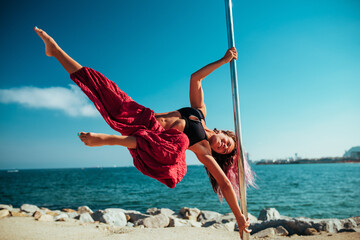 Young beautiful woman pole dancing on sea and sky background