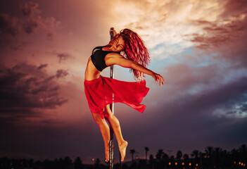 Young beautiful woman pole dancing on twilight sky and city silhouettes background