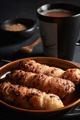 Traditional colombian food, Tequeño or Baked Cheese Stick on a brown plate and black napkin served on a dark table with hot chocolate drink, Dark food lighting