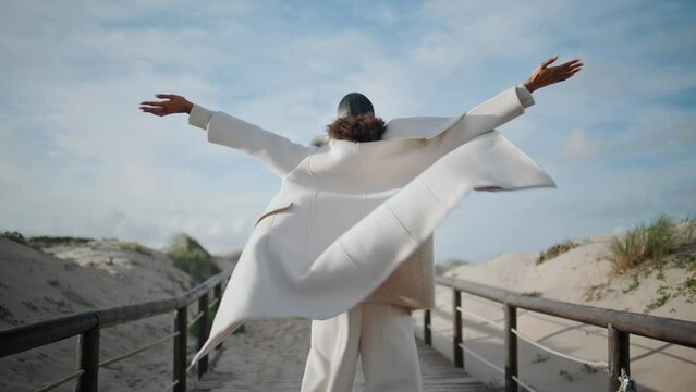 Girl spread arms open at windy beach rear view. Relaxed woman enjoying moment