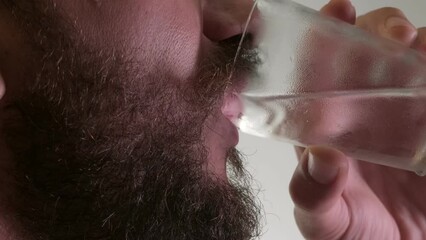 This video captures a close-up of a Caucasian man with dark brown beard and mustache as he takes a refreshing sip of cold water, set against a clean, white background. Every detail, from the beads of 