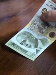 A close-up shot of a 2000 Serbian dinar banknote. A person holds a banknote in his hand