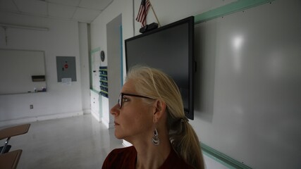 Closeup of sad unhappy teacher with US flag in an empty classroom with the lights turned off during...