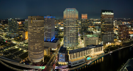 Fototapeta premium View from above of illuminated skyscraper buildings, pedestrian riverwalk and street traffic in downtown of Tampa city in Florida, USA. American megapolis with business financial district at night