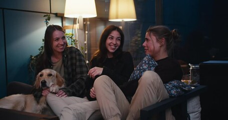 Happy trio of girls are sitting on the couch chatting and having fun. Active communication, cheerful and cozy evening