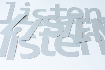 the word "listen" machine-cut from three different font-types and arranged on blank paper (photographed at an oblique angle under available light)