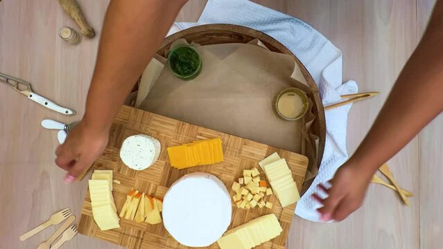 4K resolution time-laps, preparing cheese and crackers board  with fruit and prosciutto on a large round wood platter on top of wax paper.