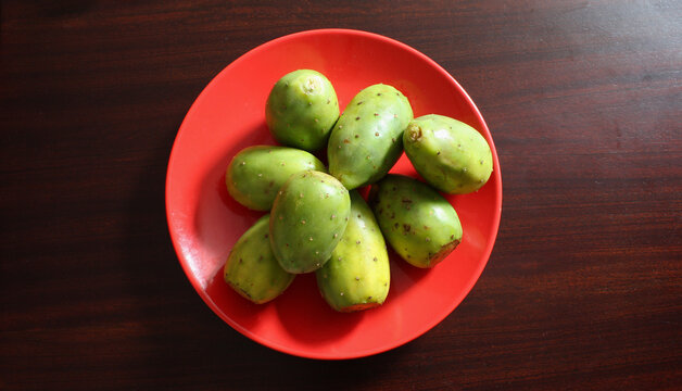 Plato rojo con tunas verdes sobre superficie de madera cafe. 