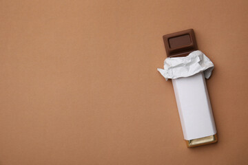 Tasty chocolate bar in package on light brown background, top view. Space for text