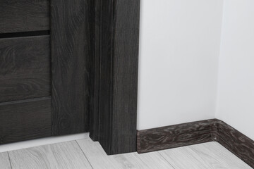 Black wooden plinth with connector on laminated floor near door indoors