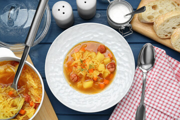 Delicious sauerkraut soup with smoked sausages served on blue wooden table, flat lay