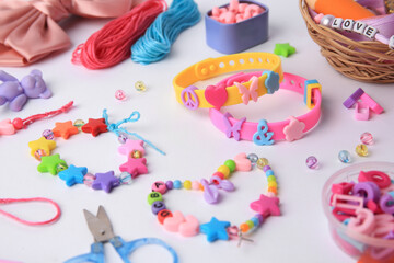 Kid's handmade beaded jewelry and different supplies on white background, closeup