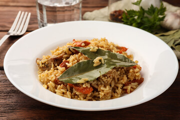 Delicious pilaf and bay leaves on wooden table, closeup