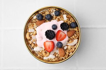 Tasty granola, yogurt and fresh berries in bowl on white tiled table, top view. Healthy breakfast