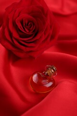 Heart shaped bottle of love potion and rose flower on red fabric