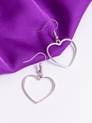 Earrings in the form of hearts. Costume jewelry for girls. Earrings on white and purple fabric background