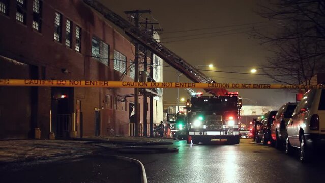 Caution tape and a fire truck with flashing lights and extended ladder at night in the snow