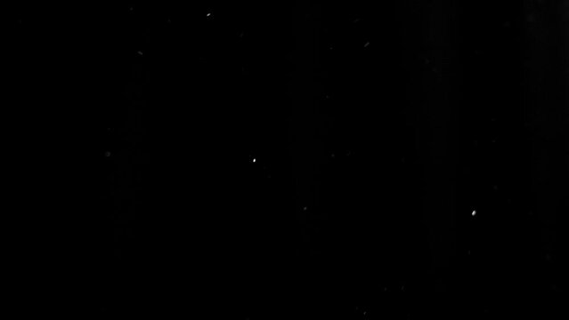 Dust particles swirling in the air in front of a black background. Fine grain is moving in random directions. This footage can be used as an overlay asset or as texture.