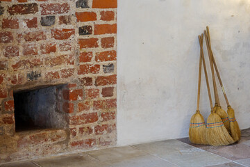 Group of brooms lean against white wall next to old brick wall and chimney. 