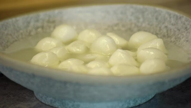 Balls of mozzarella cheese. A hand puts a plate of cheese on the table.
