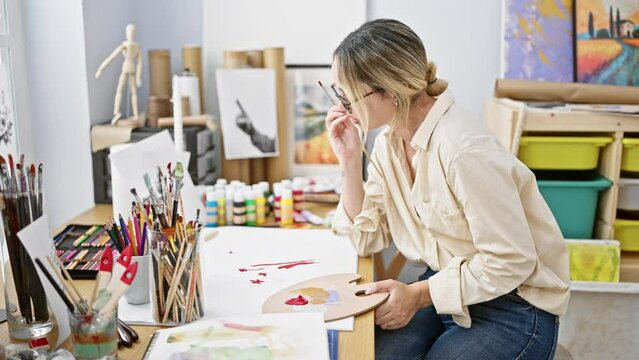 Young blonde woman artist drawing on paper thinking at art studio