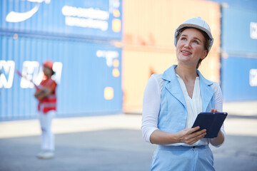 businesswoman wearing safety helmet and working on tablet in containers warehouse storage