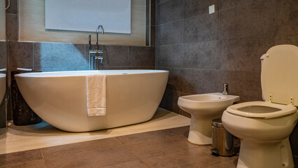 The interior of a modern bathroom. A white towel draped over the edge of a large oval acrylic...