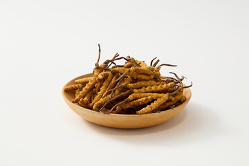 Dried Cordyceps Sinensis contained inside a wooden dish. White background. Cordyceps is often used...