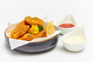 Fish and Chips (battered fish and fries potato) served in a large bowl decorated with flowers and parsley and dipping sauce (ketchup and mayonnaise) isolated on white background.