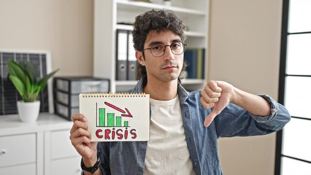 Young hispanic man business worker holding crisis banner doing thumb down gesture at office