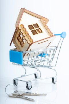 A wooden house in a supermarket cart and the keys to the apartment. White background.