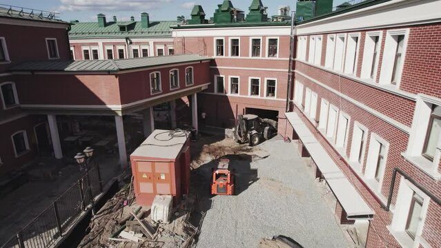 Construction team renovating courtyard of public building with machinery. Excavator carrying materials for renovation premise of structure