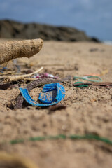 Polluted beach filled with plastic bottles fishing nets, slippers, bottlecaps and various other plastic junk with ocean waves in the background.