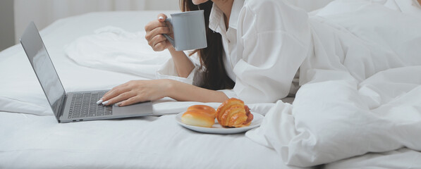 Happy young female in casual clothes smiling and looking at camera while using laptop on bed in bedroom at home