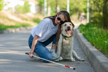 Blind young woman cuddling with guide dog on a walk outdoors. 