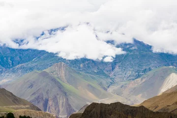 Papier Peint photo Dhaulagiri Dark Dramatic Desert Landscape with Foggy Mountains and Distant Houses in Muktinath, Mustang, Nepal