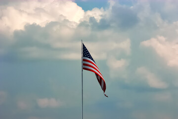 The USA American flag waving in the wind against a cloudy blue sky. The flag is bright and vibrant. The flag is dwindling at its edge.