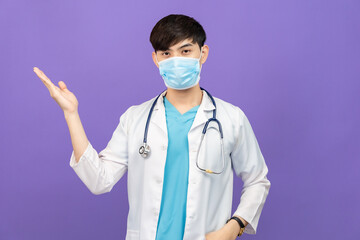 Young asian man  surgeon happy smile indicate finger empty space with protective mask isolated color background.