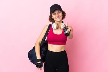 Young sport woman with sport bag over isolated background smiling and showing victory sign