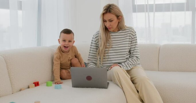 young mother, little child relaxing on cozy couch with laptop, watching funny video clips at social media Young single mom having fun with little son using app on pc Slow motion, online free education