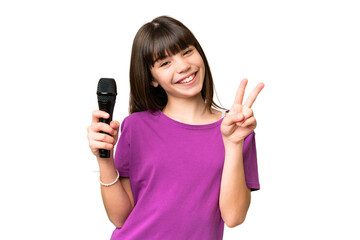 Little singer girl picking up a microphone over isolated background smiling and showing victory sign