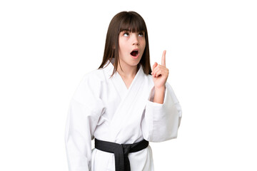 Little Caucasian girl doing karate over isolated background thinking an idea pointing the finger up