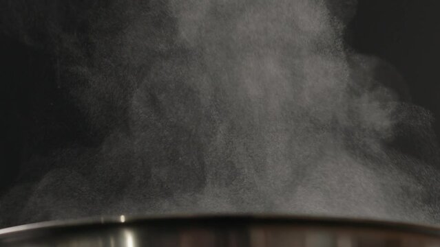 Slow motion steam rising from boiling water in pot over black background