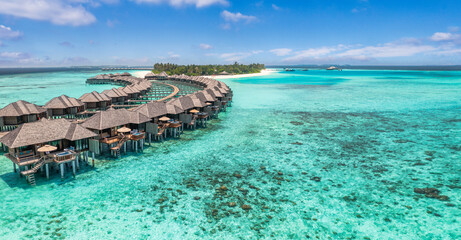 Aerial view of Maldives island, luxury water villas wooden pier path resort. Beautiful sky and ocean bay beach background. Summer vacation travel destination. Paradise aerial landscape panoramic coast