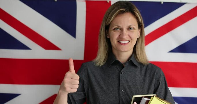 Young woman salutes language learning with thumb up. English teacher stands in front of British flag and encourages students to study