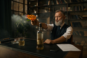 Brutal senior man shooting toy gun while sitting at table with alcohol drink