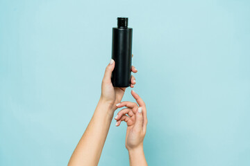 Hands hold black bottle of cosmetic product for skin on blue background