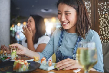 Foto op Plexiglas Sushi bar Japanese woman, restaurant and eating sushi with smile, chopsticks and excited for fine dining at party. Asian friends, fish and healthy with culture, traditional or fast food in diner, bar or shop