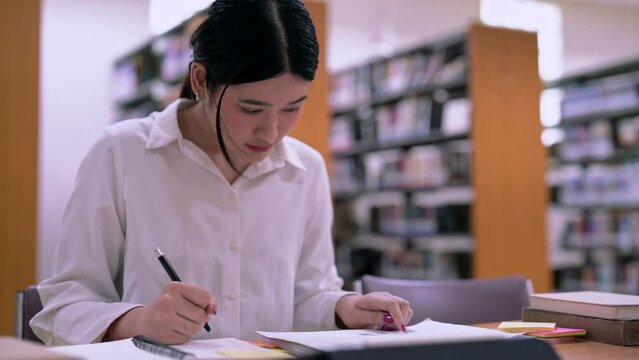 Young Asian Female student college do homework and reading a book for final exam at library, education concept.